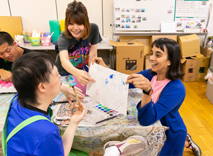 写真：笑顔でアートを掲げるライラさんと支援員